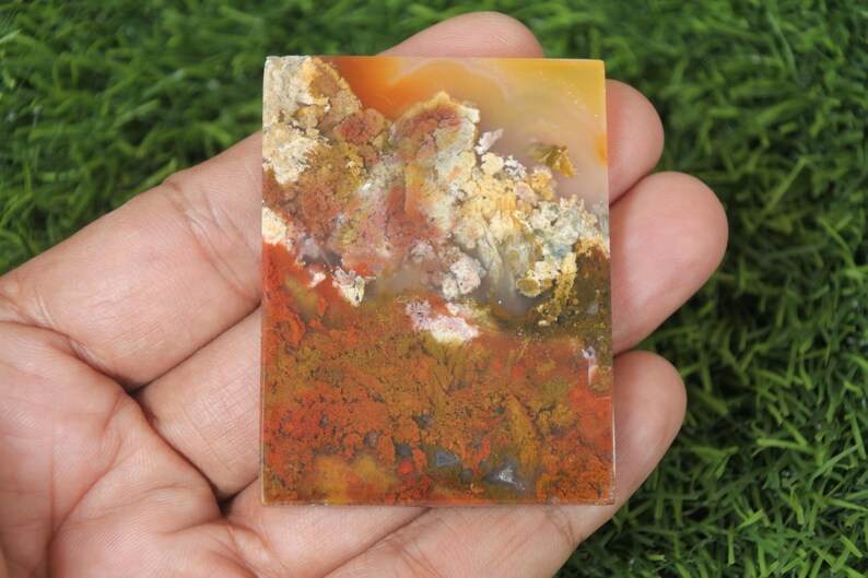 K&ouml;nnte beinhalten: Ein rechteckiges St&uuml;ck Achat mit einer Vielzahl von Farben, darunter Orange, Rot, Gelb und Braun. Der Achat hat ein wirbelndes Muster und eine glatte, polierte Oberfl&auml;che.