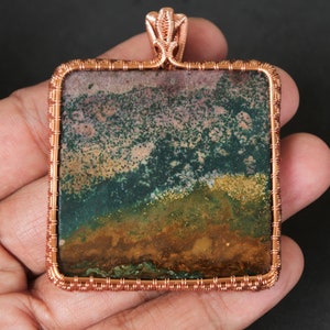 May include: A square copper wire wrapped pendant featuring a green, brown, and pink agate stone.
