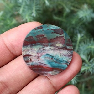 May include: A round, flat, green, red and white agate cabochon with a swirling pattern.