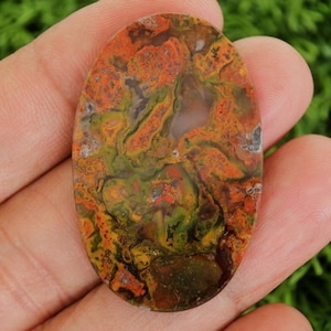 Op de afbeelding: Een ovaalvormige edelsteen met een levendige mix van kleuren. De steen heeft een combinatie van oranje, groene en bruine tinten, waardoor een uniek en natuurlijk patroon ontstaat. Het gepolijste oppervlak benadrukt de ingewikkelde details van de steen.