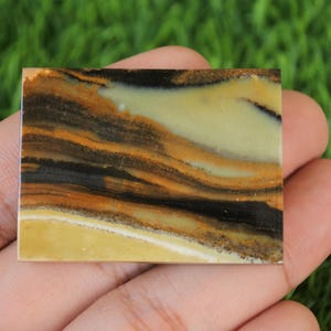 May include: A close-up of a polished, rectangular slab of banded agate with brown, black, and white stripes. The agate is smooth and has a natural, organic pattern.