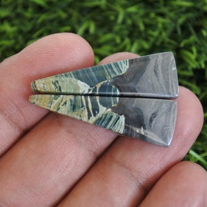 May include: Two polished gemstone pieces, triangular in shape. The stones display a mix of blue, green, and grey, with a marbled pattern. The edges are smooth, giving a natural appearance. Each piece is approximately 3 cm long.