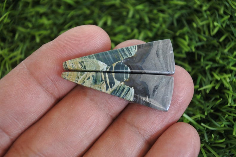 May include: Two polished gemstone pieces, triangular in shape. The stones display a mix of blue, green, and grey, with a marbled pattern. The edges are smooth, giving a natural appearance. Each piece is approximately 3 cm long.
