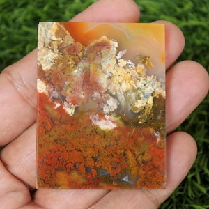 K&ouml;nnte beinhalten: Ein rechteckiges St&uuml;ck Achat mit einer Vielzahl von Farben, darunter Rot, Orange, Gelb, Braun und Wei&szlig;. Der Achat hat ein wirbelndes Muster und ist durchscheinend.