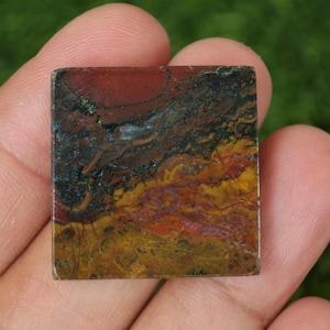 May include: A square piece of polished agate with a red, brown, yellow, and black pattern. The agate has a smooth, polished surface.
