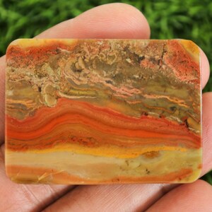 Puede incluir: Una piedra rectangular con un patr&oacute;n en capas de tonos naranja, rojo, amarillo y marr&oacute;n. La piedra tiene esquinas redondeadas y una superficie pulida, mostrando los colores y texturas naturales.