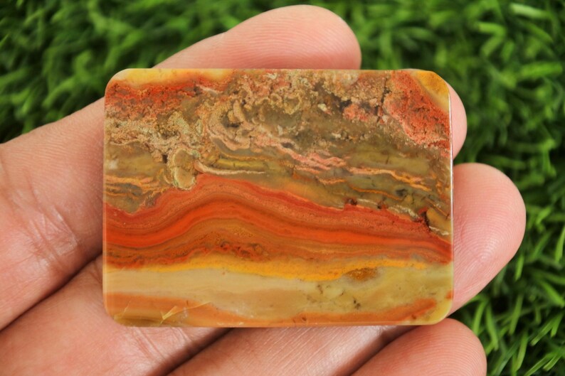 Puede incluir: Una piedra rectangular con un patr&oacute;n en capas de tonos naranja, rojo, amarillo y marr&oacute;n. La piedra tiene esquinas redondeadas y una superficie pulida, mostrando los colores y texturas naturales.