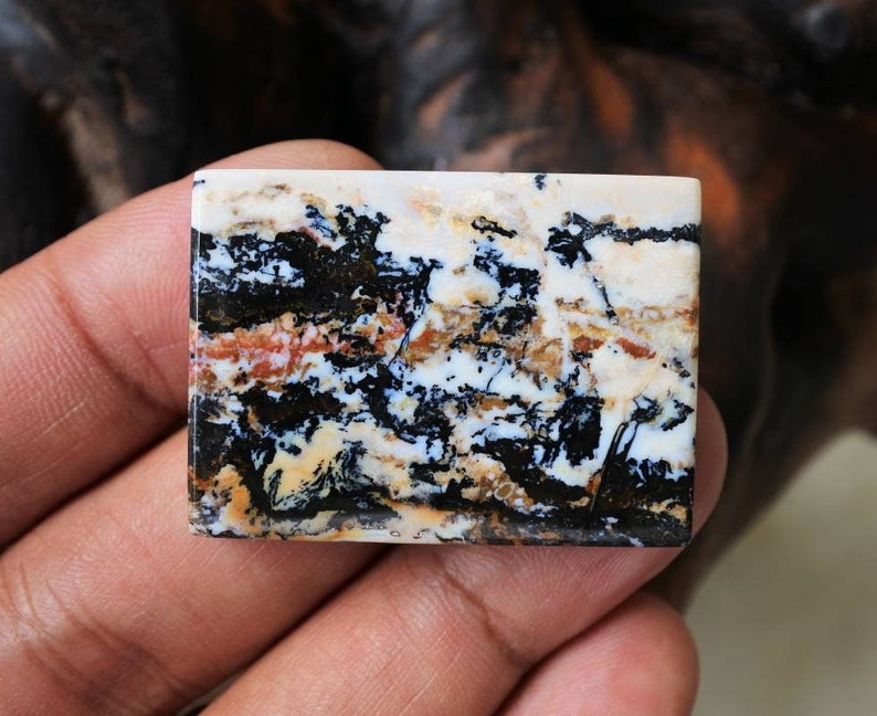 Puede incluir: Un cabuj&oacute;n rectangular de &aacute;gata blanco, negro y marr&oacute;n con un patr&oacute;n abstracto &uacute;nico. La piedra tiene una superficie pulida y mide aproximadamente 5 cm de largo.