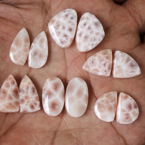 Op de afbeelding: Een verzameling van acht roze en witte agaat cabochons met een uniek, organisch patroon. De cabochons zijn in verschillende vormen, waaronder druppel, ovaal en driehoekig.