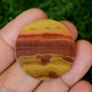 Może przedstawiać: Okrągły, polerowany kamień z warstwowym wzorem w kolorze czerwonym, pomarańczowym i żółtym. Kamień ma gładkie, błyszczące wykończenie.