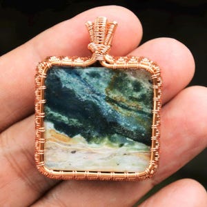 May include: A copper wire wrapped pendant featuring a square green, white, and brown agate stone.
