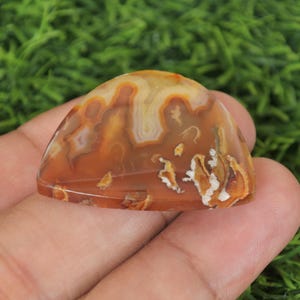 May include: A brown and white agate cabochon with a unique pattern. The cabochon is smooth and polished, with a slightly rounded shape.