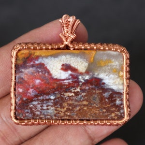 May include: A copper wire wrapped pendant featuring a colourful agate stone with red, white, yellow, and brown patterns.