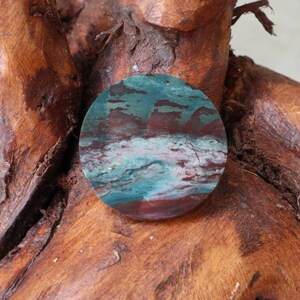 May include: A round, polished stone with a swirling pattern of blue, green, and red colours. The stone is set against a brown wooden background.