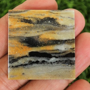 May include: Square stone tile featuring a layered pattern in yellow, black, and white. The polished surface of the tile gives it a natural, earthy look. The tile, held in a hand, displays its size and texture. The tile measures approximately 5 cm x 5 cm.