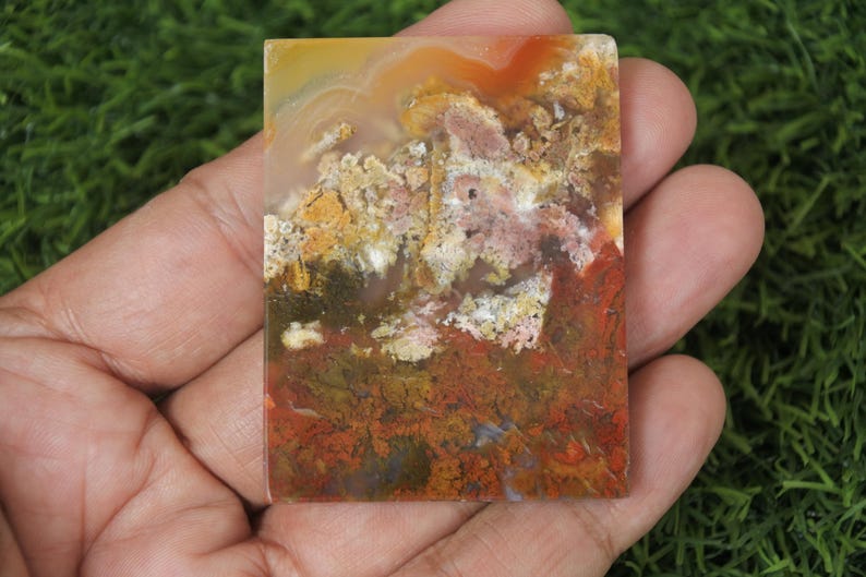 K&ouml;nnte beinhalten: Nahaufnahme einer bunten Achatplatte mit Schattierungen von Rot, Orange, Gelb, Wei&szlig; und Braun. Der Achat hat ein nat&uuml;rliches, organisches Muster.