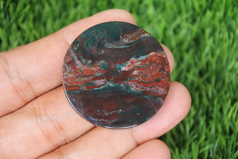 May include: A round, polished stone with a swirling pattern of deep red, dark green, and brown hues. The stone's surface has a glossy finish, and the colors blend together in a natural, organic design. This decorative stone is ideal for jewelry making or display.