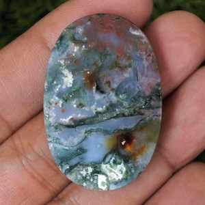 Może przedstawiać: Owalny kamień szlachetny o unikalnym wzorze kolorów. Kamień charakteryzuje się mieszanką odcieni niebieskiego, zielonego, brązowego i czerwonego, tworząc naturalny, artystyczny wygląd. Wypolerowana powierzchnia podkreśla skomplikowane detale kamienia.