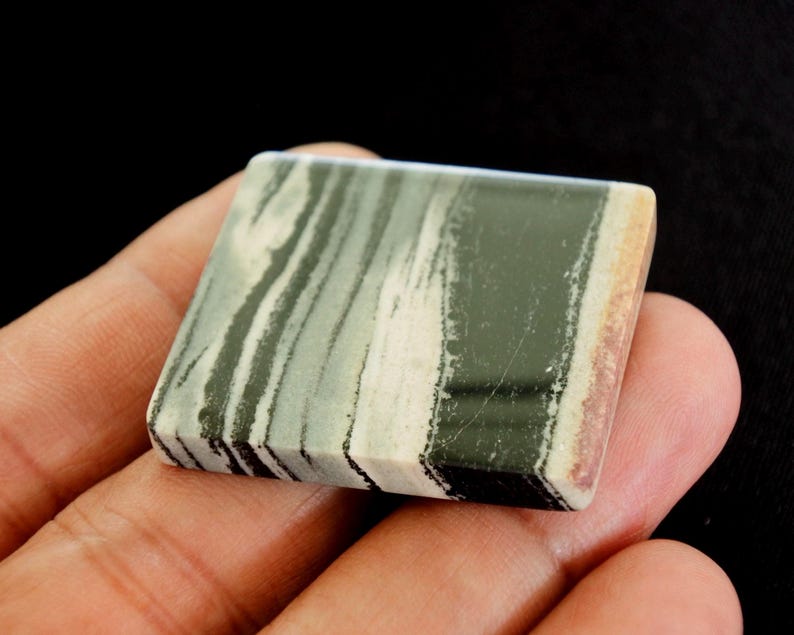 May include: A square stone with a layered pattern of green, white, and black. The stone has a polished surface and a natural appearance. The edges show a mix of colours, including tan and reddish-brown.