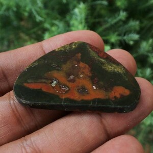 K&ouml;nnte beinhalten: Ein polierter Stein mit einem einzigartigen Muster in Gr&uuml;n-, Orange- und Braunt&ouml;nen. Der Stein ist dreieckig geformt und hat eine glatte, polierte Oberfl&auml;che.