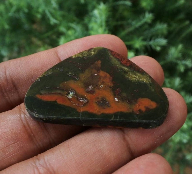 K&ouml;nnte beinhalten: Ein polierter Stein mit einem einzigartigen Muster in Gr&uuml;n-, Orange- und Braunt&ouml;nen. Der Stein ist dreieckig geformt und hat eine glatte, polierte Oberfl&auml;che.