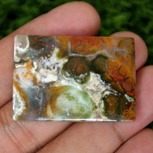 May include: A colourful agate cabochon with shades of green, brown, orange, and white. The stone has a unique pattern of swirls and veins.