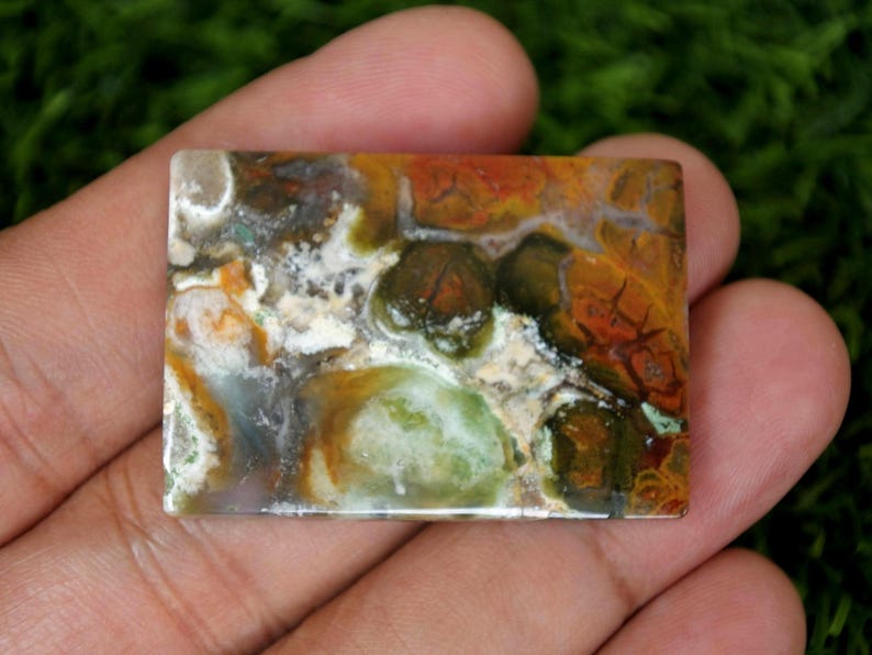 K&ouml;nnte beinhalten: Ein bunter Achat-Cabochon in Gr&uuml;n-, Braun-, Orange- und Wei&szlig;t&ouml;nen. Der Stein hat ein einzigartiges Muster aus Wirbeln und Adern.