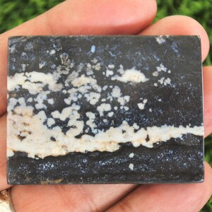 May include: A rectangular stone slab with a dark grey base, featuring white and beige patterns. The stone has a layered appearance, with a prominent white band across the centre and speckled details.