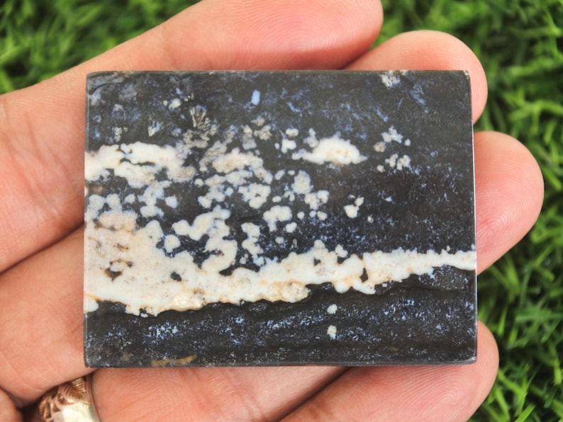 May include: A rectangular stone slab with a dark gray base, featuring white and beige patterns. The stone has a layered appearance, with a prominent white band across the center and speckled details.
