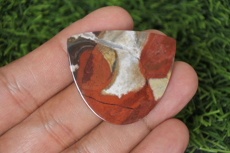 Op de afbeelding: Een rode, witte en bruine agaat cabochon met een uniek, swirlend patroon. De cabochon is traanvormig en heeft een glad, gepolijst oppervlak.