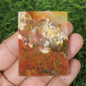 K&ouml;nnte beinhalten: Eine polierte, rechteckige Agatscheibe mit einem bunten Muster aus Rot, Orange, Gelb und Wei&szlig;. Der Achat hat ein nat&uuml;rliches, organisches Aussehen.