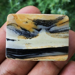 Puede incluir: Una pieza rectangular de ágata bandeada pulida con rayas negras, blancas y amarillas. El ágata tiene una superficie lisa y pulida y es una piedra natural.