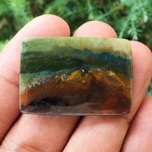May include: A rectangular green, brown, and white agate cabochon with a layered pattern. The cabochon is polished and has a smooth surface.