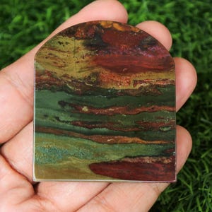 May include: A polished, green, brown, and red agate stone with a layered, banded pattern. The stone is shaped like an arch and has a smooth, polished surface.