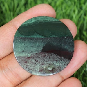 May include: A round, green and black, polished, cabochon stone with a layered pattern.