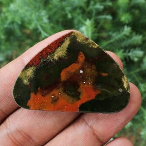 K&ouml;nnte beinhalten: Ein gr&uuml;ner, roter und goldener Achat-Cabochon mit einem einzigartigen Muster. Der Cabochon ist ein Naturstein und hat eine glatte, polierte Oberfl&auml;che.