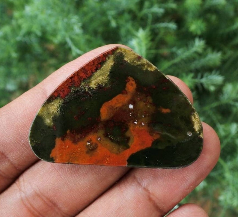 K&ouml;nnte beinhalten: Ein gr&uuml;ner, roter und goldener Achat-Cabochon mit einem einzigartigen Muster. Der Cabochon ist ein Naturstein und hat eine glatte, polierte Oberfl&auml;che.