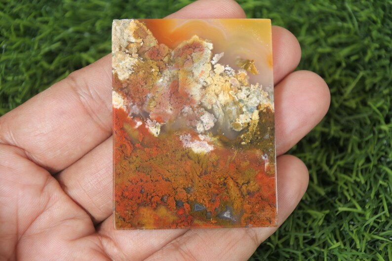 K&ouml;nnte beinhalten: Ein polierter Achat-Cabochon mit einem farbenfrohen Muster aus Rot, Orange, Gelb und Braun. Der Stein hat ein nat&uuml;rliches, organisches Aussehen.