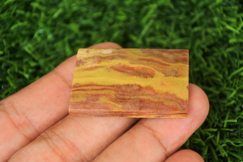 Pode incluir: Um close-up de um caboch&atilde;o de &aacute;gata com faixas amarelas, vermelhas e marrons. O caboch&atilde;o &eacute; liso e polido, com um padr&atilde;o natural e org&acirc;nico.