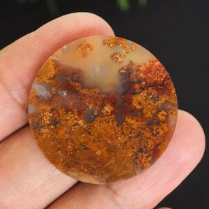 Peut inclure: Une pierre précieuse ronde et polie avec un motif unique. La pierre présente un mélange de couleurs chaudes, notamment des nuances d'orange, de marron et de crème. Le motif complexe ressemble à un paysage ou à une formation naturelle.