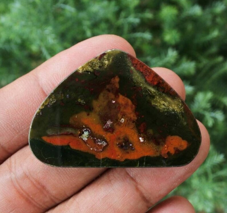 K&ouml;nnte beinhalten: Ein gr&uuml;ner, orangefarbener und brauner Achat-Cabochon mit einem einzigartigen Muster. Der Cabochon ist ein Naturstein und hat eine glatte, polierte Oberfl&auml;che.