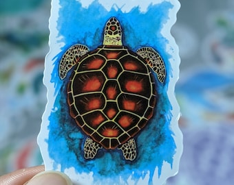 May include: A watercolor sticker of a sea turtle swimming in blue water. The turtle has a brown shell with orange accents and is facing upwards.