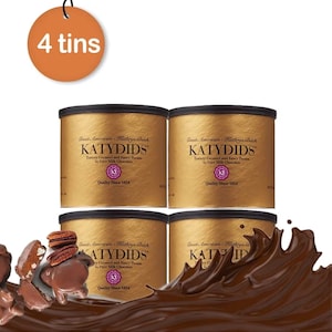 May include: Four gold-colored cylindrical tins labeled Katydids, featuring buttery caramel, fancy pecans, and pure milk chocolate. An orange circular tag at the top reads 4 tins. A splash of liquid chocolate surrounds the base with pecan pieces.