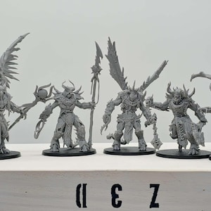 May include: Five gray fantasy miniatures of demonic figures with wings, horns, and weapons. Each figure stands on a black base. The figures are arranged in a row on a white surface. The text "II E Z" is printed on the surface.