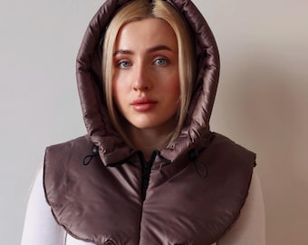 May include: A dark brown, quilted, puffer-style hood with a rounded shape that covers the head and shoulders. The hood features a black front zipper closure and two black adjustable drawstrings with toggles at the neck for a secure fit.