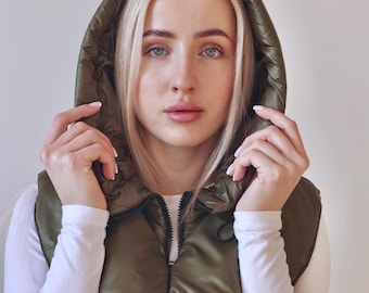 May include: An olive green quilted hood accessory featuring a smooth, water-resistant fabric finish. This detachable hood includes a front zipper closure and an adjustable drawstring cord, providing a structured, padded layer for the head and neck area.