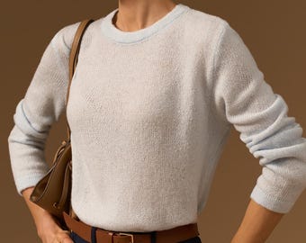 May include: A light blue long-sleeve crew neck sweater with a fine knit texture, paired with dark navy trousers, a brown leather belt with a gold-tone buckle, and a brown leather shoulder bag. The sweater features a ribbed collar and cuffs.
