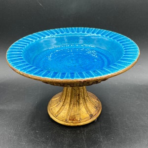 May include: A blue ceramic pedestal dish with a gold base. The dish has a scalloped edge and a smooth, glazed surface.