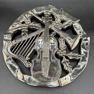 May include: Silver Christmas ornament featuring a violin, harp, trumpet, and holly leaves.