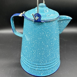 May include: A blue enamel camping coffee pot with a white speckled design and a wire handle. The pot has a blue rim and a spout.